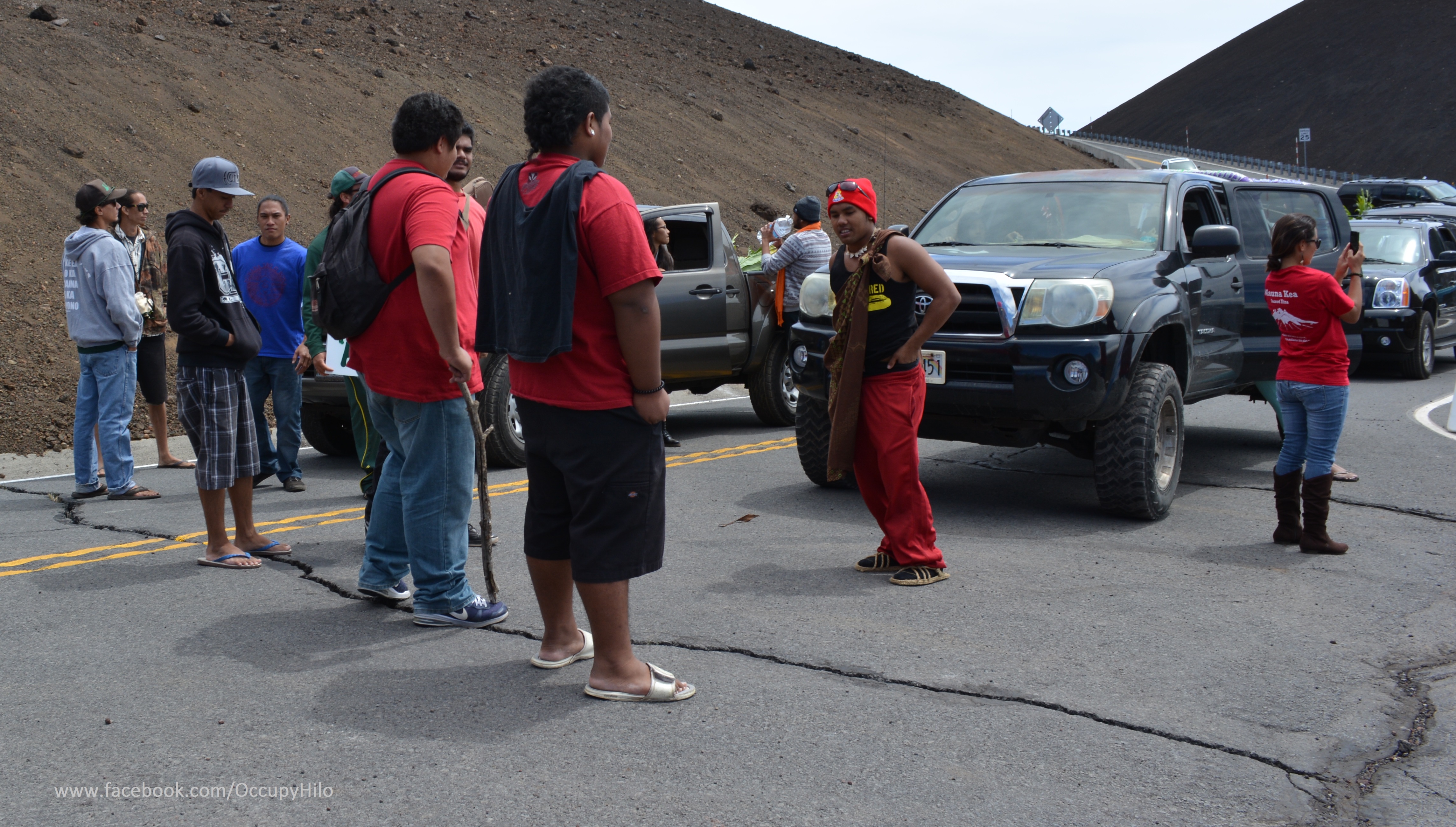 A row of people face off with a line of cars at a road blockade.