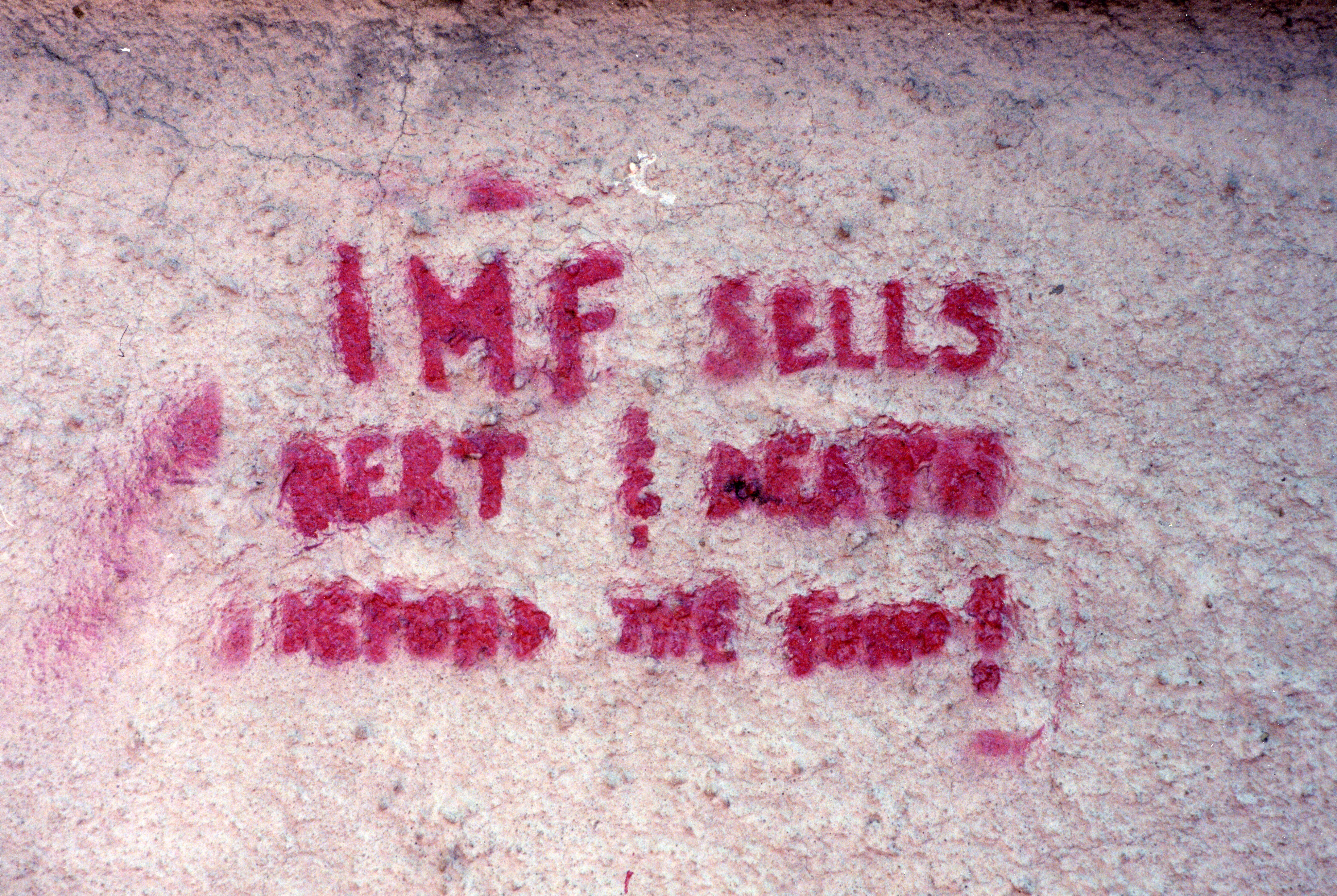 Pink stenciled letters on a sidewalk read: “IMF SELLS DEBT & DEATH. DEFUND THE FUND!”