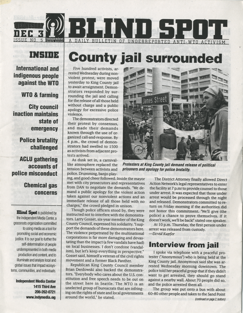The cover of a news publication, “BLIND SPOT.” The article is titled “County Jail Surrounded.” The accompanying photograph shows a crowd of people gathered outside a courthouse near a street sign that reads “James Street.”